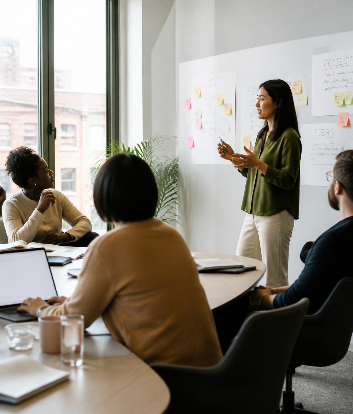 Facilitadora conduzindo um workshop com um pequeno grupo de profissionais em uma sala de reunião